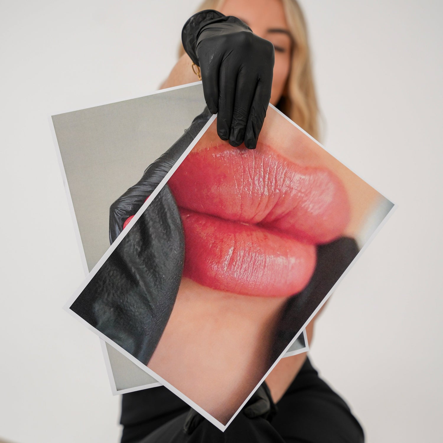 Person holding a photo of lips with a black glove on a neutral background