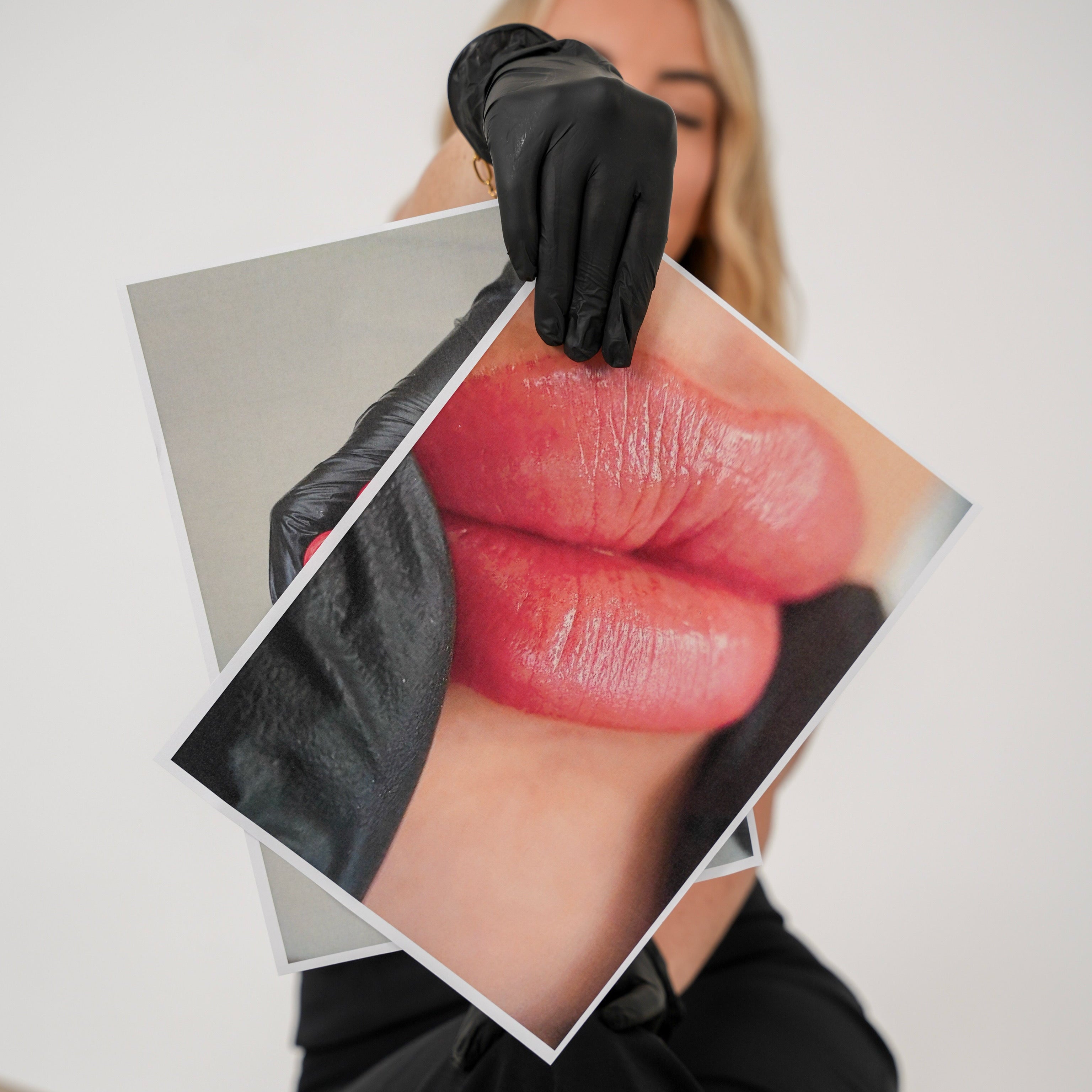 Person holding a photo of lips with a black glove on a neutral background