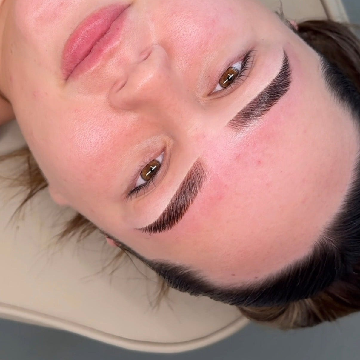 Person with exaggerated makeup, including thick eyebrows and pink lipstick, lying on a surface.